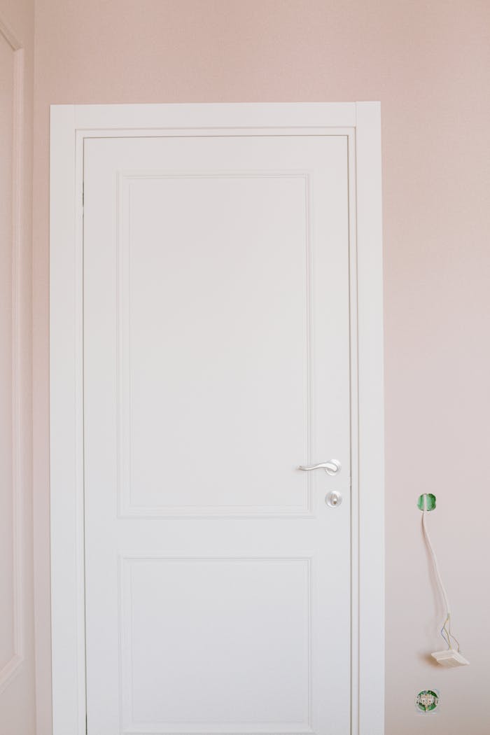 gallery-2 A white door with handle in a pink-walled room under renovation, minimalistic style.
