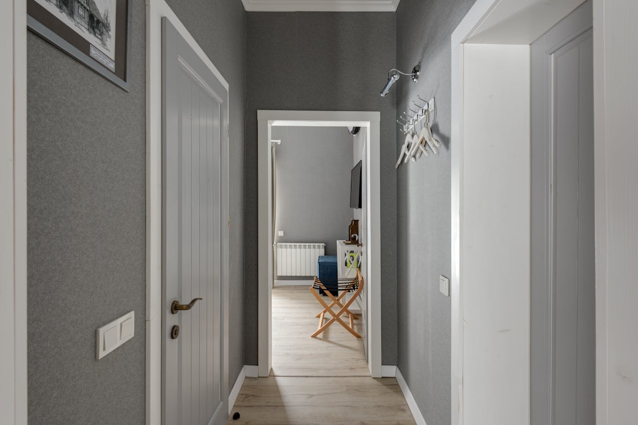 Spacious hallway with grey walls, wooden doors and white hangers, leading into a modern room.